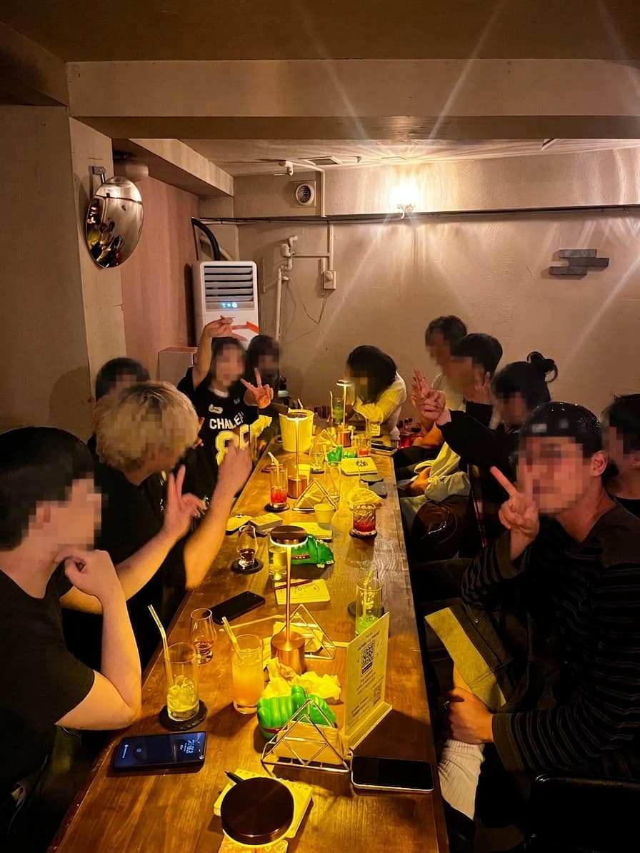 경기도 의정부시 제주도트 혼술바 의정부점 바(Bar)의 긴 원목 다찌석. 노란색 조명 아래 다양한 색상의 칵테일이 놓여 있으며 1인 좌석에 모여 앉아 혼술을 즐기는 상황.