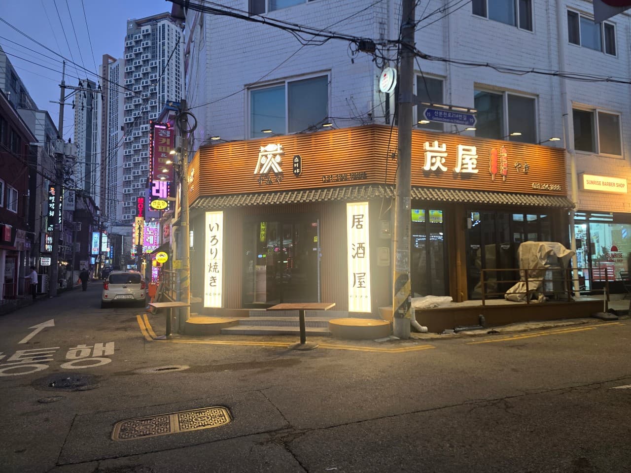 경기도 군포시 이자카야 스미야 경기 군포. 노란 조명이 켜진 목재 외벽과 1인 혼술용 다찌석이 있는 건물 1층 코너의 저녁 시간대 상황.