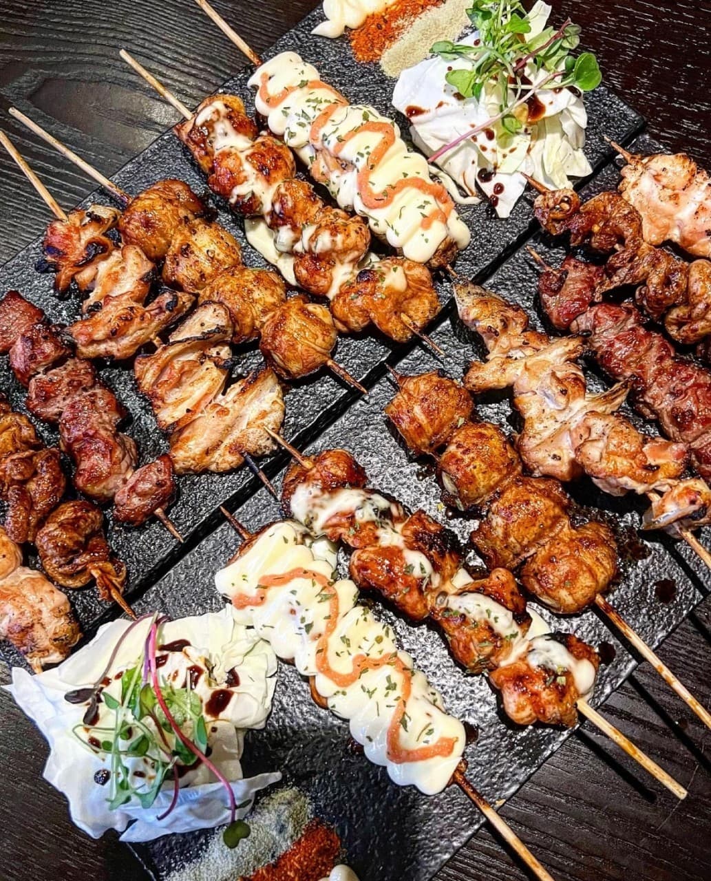 경기도 안양시 잔잔 범계역점 이자카야 다찌석 조명 아래 놓인 혼술 메뉴. 노릇한 닭꼬치와 마요네즈 소스가 얹어진 야키토리 모듬이 검은 석재판에 담겨 서빙됨.