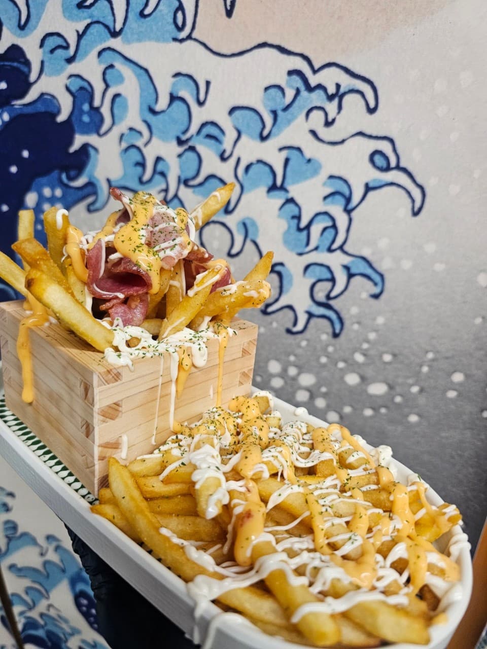 경기도 안양시 케로케로 안양점 경기 이자카야 1인 다찌석 혼술. 파도 벽화 앞 나무 상자와 접시에 소스가 듬뿍 뿌려진 베이컨 감자튀김이 놓인 구성.
