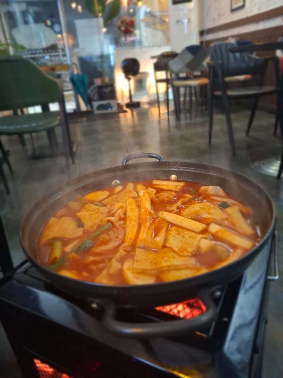 경기도 안양시 뮌헨호프 경기 안양 맥주 호프 - 실내 조명 아래 버너 위 김이 나는 떡볶이 전골과 1인석 테이블이 배치된 혼술 상황