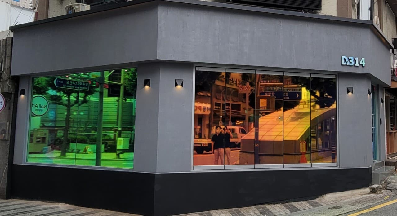경기도 안양시 바(Bar) D314 경기 안양의 무지개 빛 반사 유리창과 회색 벽면 조명이 켜진 건물 외관. 혼술을 위해 방문하는 1인 손님의 상황을 묘사함.