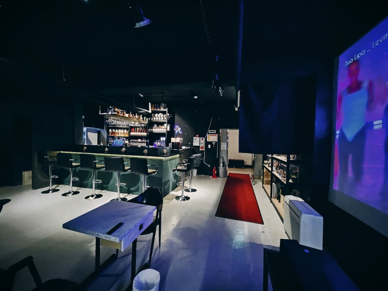 경기도 성남시 JANA BAR & PUB 바의 푸른 조명과 긴 카운터석. 혼술을 위한 다찌석과 대형 스크린이 설치된 어두운 실내에 붉은 카페트가 깔린 모습.