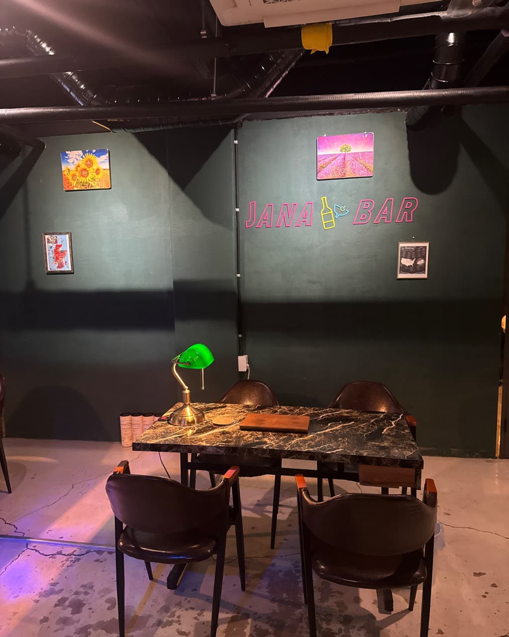 경기도 성남시 혼술 바 JANA BAR & PUB - 초록색 스탠드 조명 아래 대리석 테이블과 가죽 의자. 네온 로고가 있는 벽면 앞 1인 이용 가능 공간
