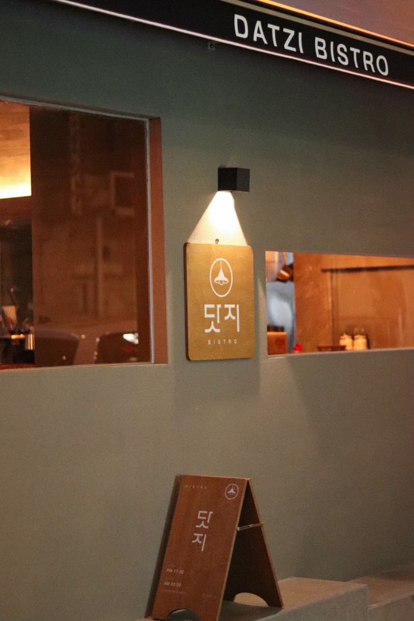 경기도 구리시 요리주점 닷지 - 핀 조명이 비추는 나무 간판과 유리창 너머 다찌석이 배치된 1인 혼술 공간의 외경