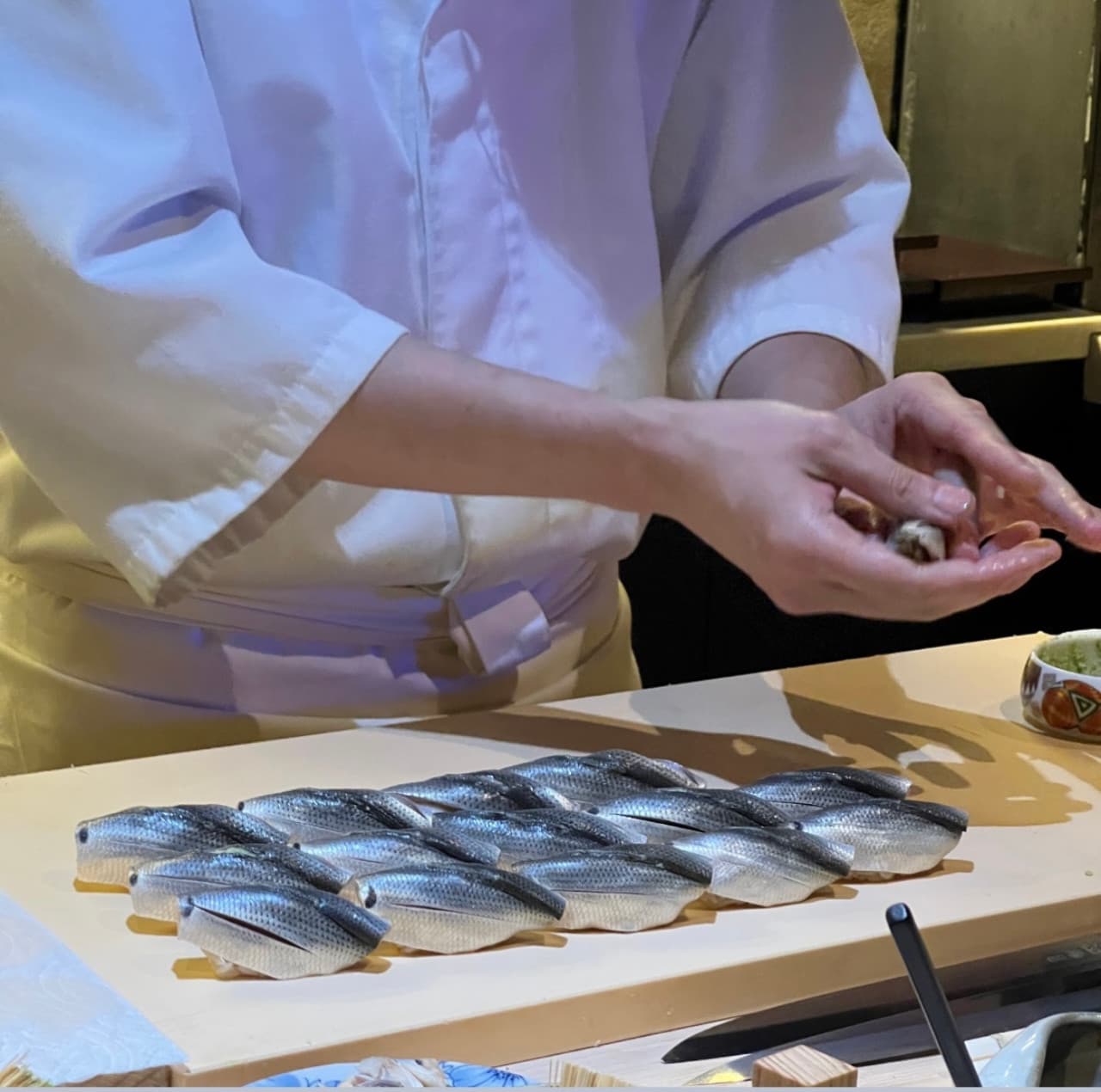 서울특별시 광진구 혼술 이자카야 류지로 - 다찌석 앞 셰프가 쥔 은빛 초밥과 도마 위 정렬된 생선 질감. 밝은 조명 아래 1인 식사 상황을 보여줌.