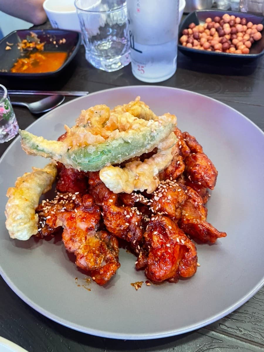전남광주통합특별시 순천시 동선주막 순천 - 조명 아래 윤기 나는 양념치킨과 바삭한 고추튀김, 증류주가 차려진 1인 다찌석의 기타 안주 혼술 상황