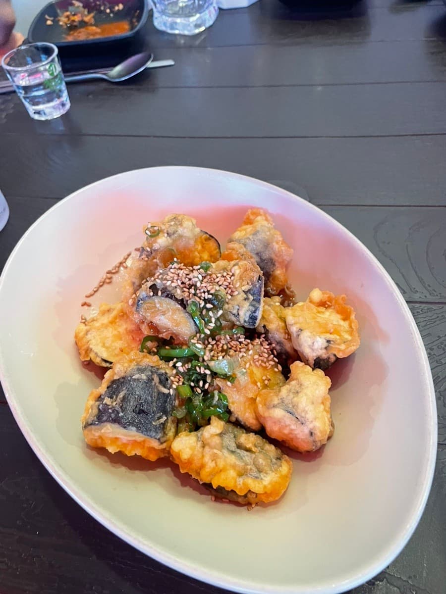 전남광주통합특별시 순천시 동선주막 순천 다찌석 1인 혼술. 바삭한 튀김옷에 깨와 파를 얹은 안주와 소주잔이 놓인 어두운 목재 테이블. 기타 주점 카테고리의 요리 질감과 조명 아래 식탁 전경.