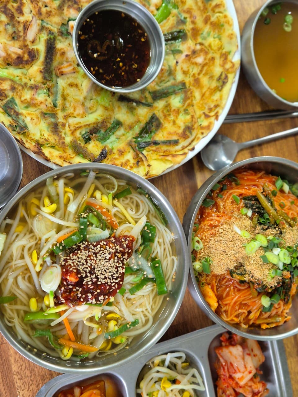 전남광주통합특별시 순천시 동선주막 순천 다찌석 조명 아래 1인 혼술 차림. 노릇한 파전과 양념 국수가 놓인 목재 테이블 위 식사 상황과 음식의 질감.