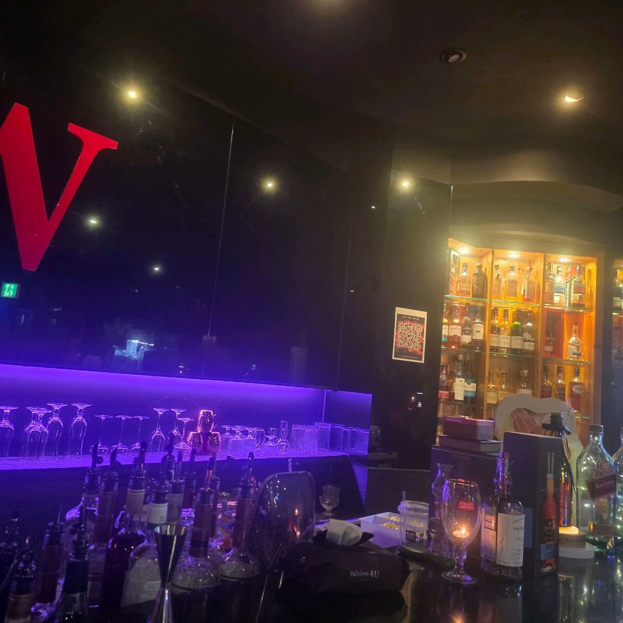 전남광주통합특별시 광양시 더블유바 전남 바(Bar)의 보라색 조명 아래 위스키 병과 글라스가 진열된 다찌석. 1인 혼술이 가능한 카운터와 조명이 밝은 술장고가 있는 내부 공간.