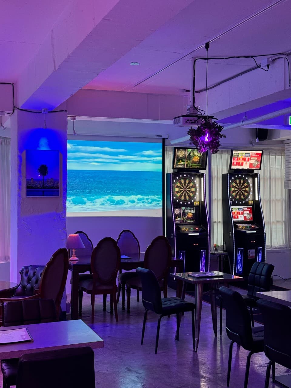 인천광역시 미추홀구 슬로우 인천 바(Bar)의 보라색 조명 아래 다트 기계와 바다 영상 스크린이 배치된 1인 혼술 테이블 좌석