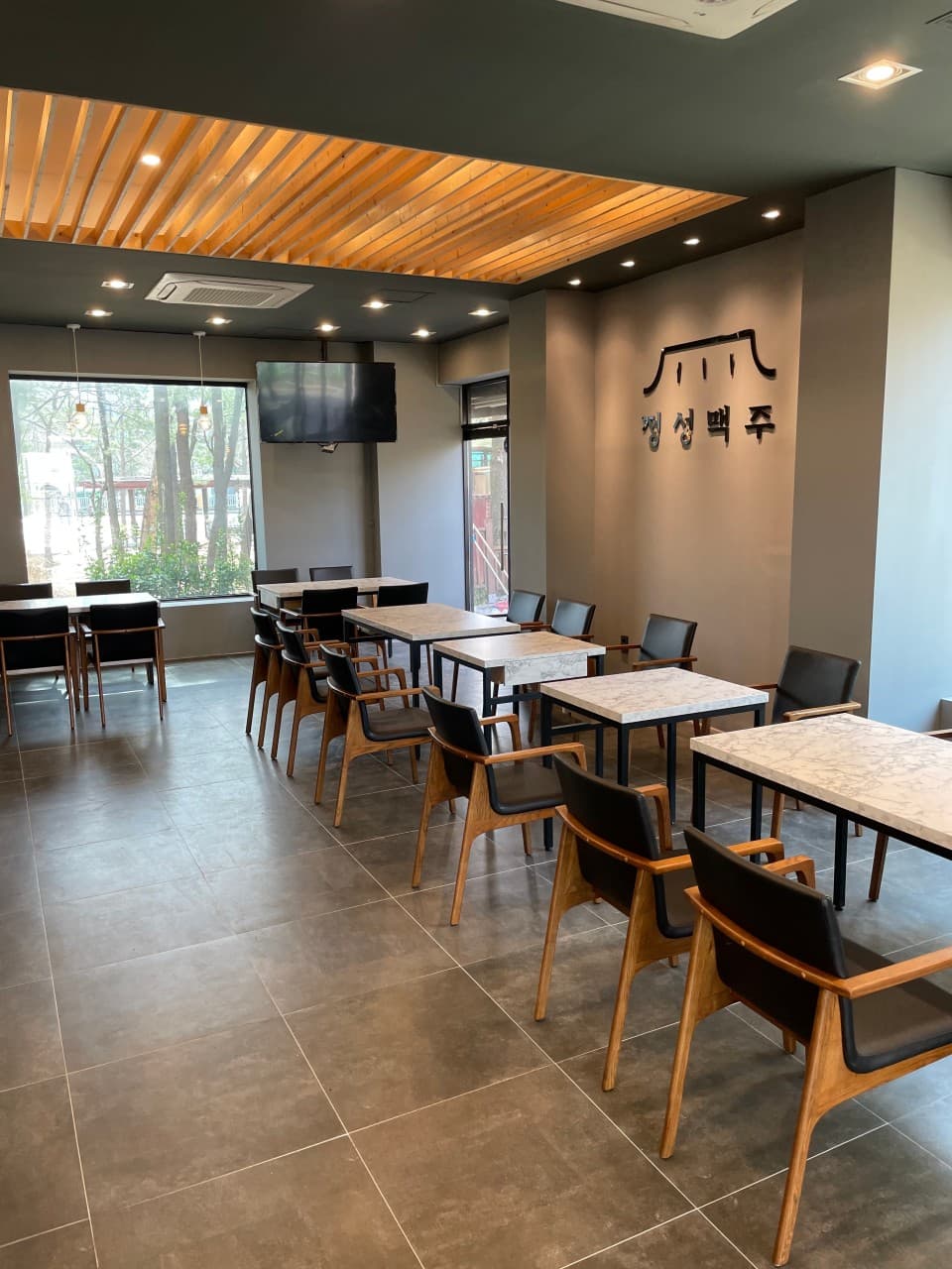 인천광역시 연수구 정성맥주 인천 맥주 호프 매장 내부. 따뜻한 핀조명 아래 대리석 테이블과 목재 의자가 정돈된 모습. 혼술 가능한 1인 좌석 분위기와 큰 창문 너머로 보이는 가로수 풍경.
