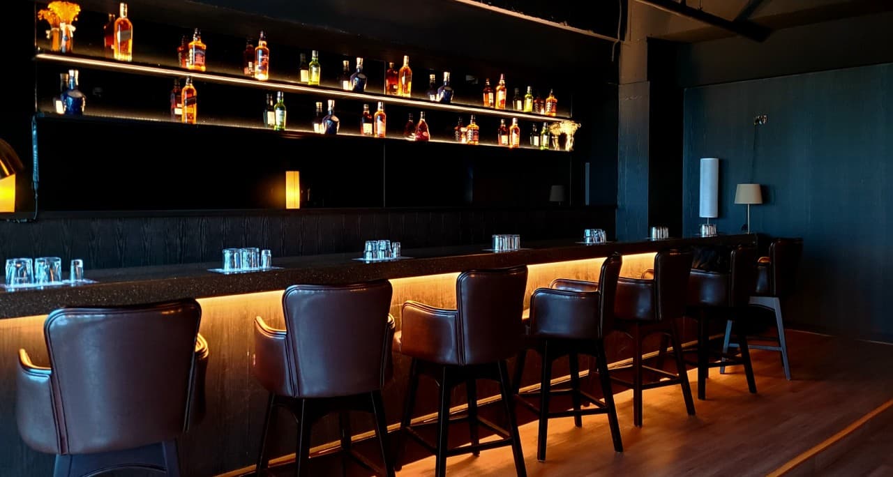 인천광역시 연수구 VIP BAR 인천 바(Bar) 내부의 오렌지색 간접 조명이 흐르는 다찌석과 가죽 소재 1인석. 벽면 가득한 위스키 병과 정갈한 유리잔이 놓인 혼술 상황.