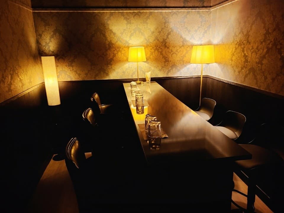 인천광역시 연수구 VIP BAR 인천 바(Bar)의 노란 스탠드 조명 아래 배치된 긴 다찌석. 패턴 벽지 앞 카운터석에 유리잔이 정렬된 혼술을 위한 1인석 공간.