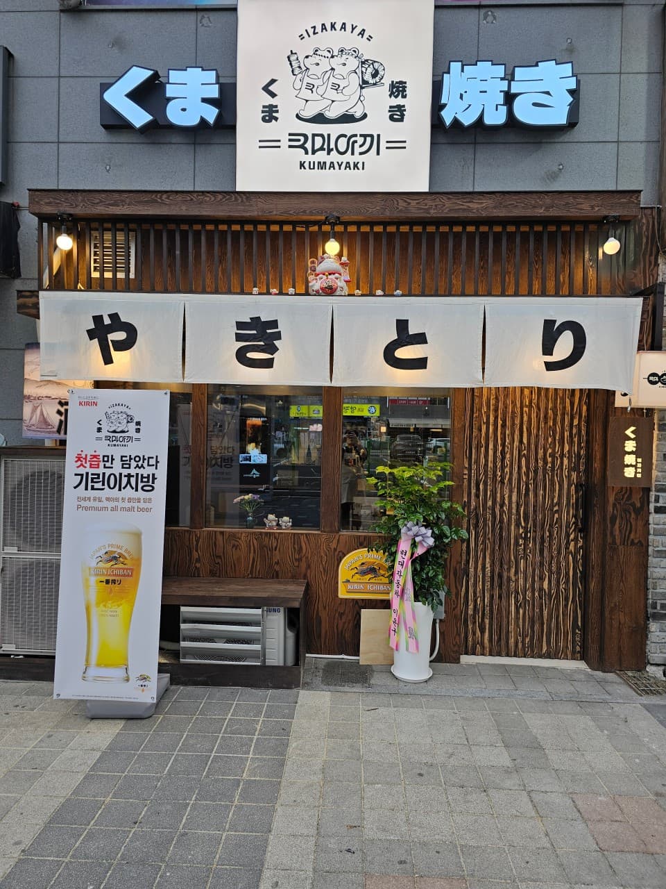 세종특별자치시 나성로 혼술 이자카야 쿠마야끼 세종 - 목재 외벽과 황색 조명 아래 야키토리 노렌이 걸린 입구와 1인 다찌석이 위치한 내부 전경