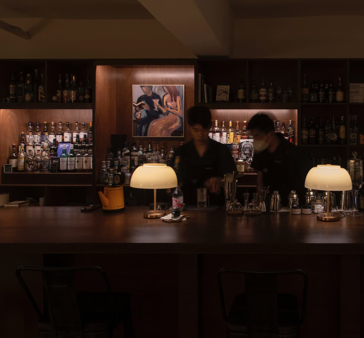 서울특별시 마포구 책바 서울 바(Bar). 노란 조명이 켜진 원목 다찌석과 벽면 가득한 술병들, 바텐더가 칵테일을 조제하는 1인 혼술 공간.