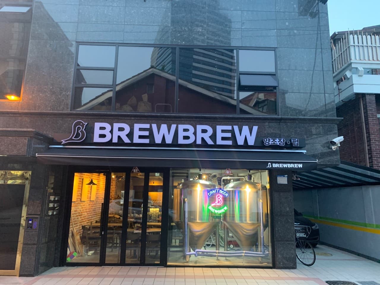 서울특별시 마포구 브루브루 서울 맥주,호프 매장. 통유리 속 대형 발효조와 전구색 조명이 비치는 다찌석에서 혼술을 즐기는 1인 펍 분위기.