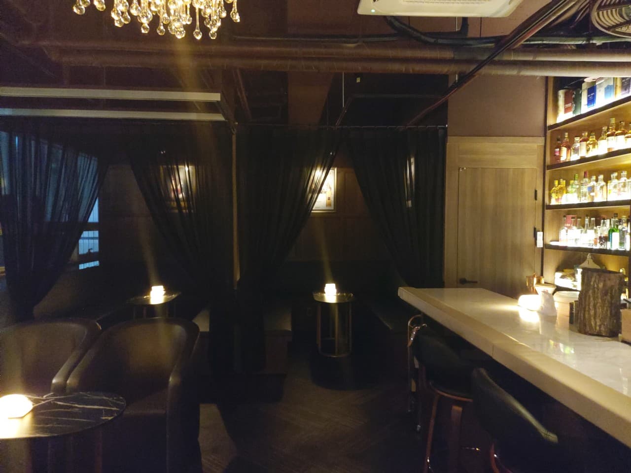 서울특별시 강서구 깔루아 서울 바(Bar) 조명 아래 길게 뻗은 다찌석과 1인 혼술용 커튼 좌석. 벽면 진열장을 가득 채운 술병들과 낮은 조도의 노란 조명이 배치된 내부 구성.