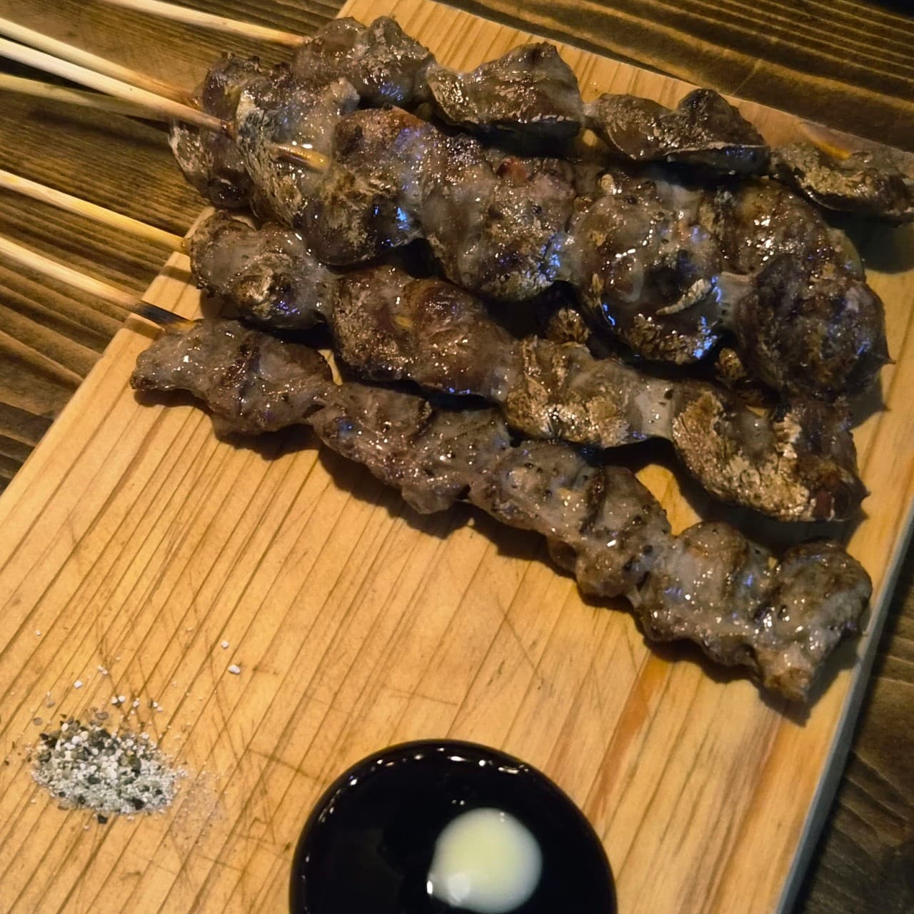 대전광역시 서구 요리주점 낭만짚불구이 대전괴정점 다찌석에서 혼술로 즐기는 짚불 꼬치구이. 어두운 조명 아래 육즙이 도는 고기 질감과 소금, 소스가 차려진 상황.