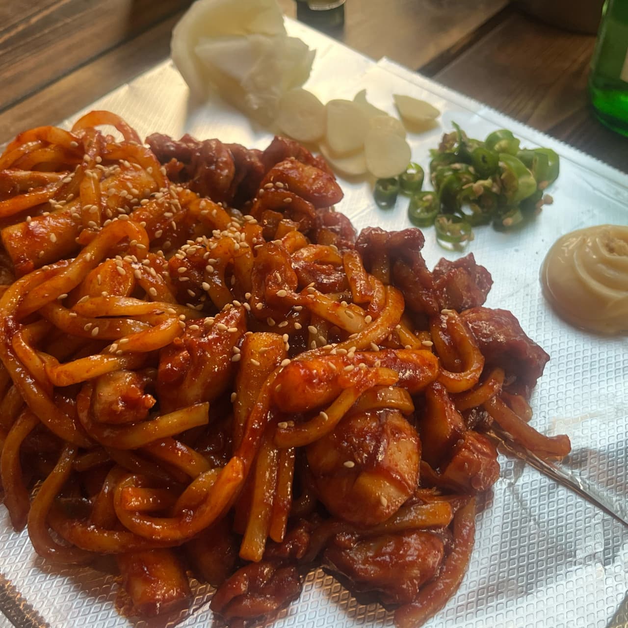 대전광역시 서구 혼술 요리주점 낭만짚불구이 대전괴정점 - 조명 아래 다찌석 은박지 위 윤기 흐르는 매콤한 볶음 요리와 마늘, 고추, 마요네즈 상차림