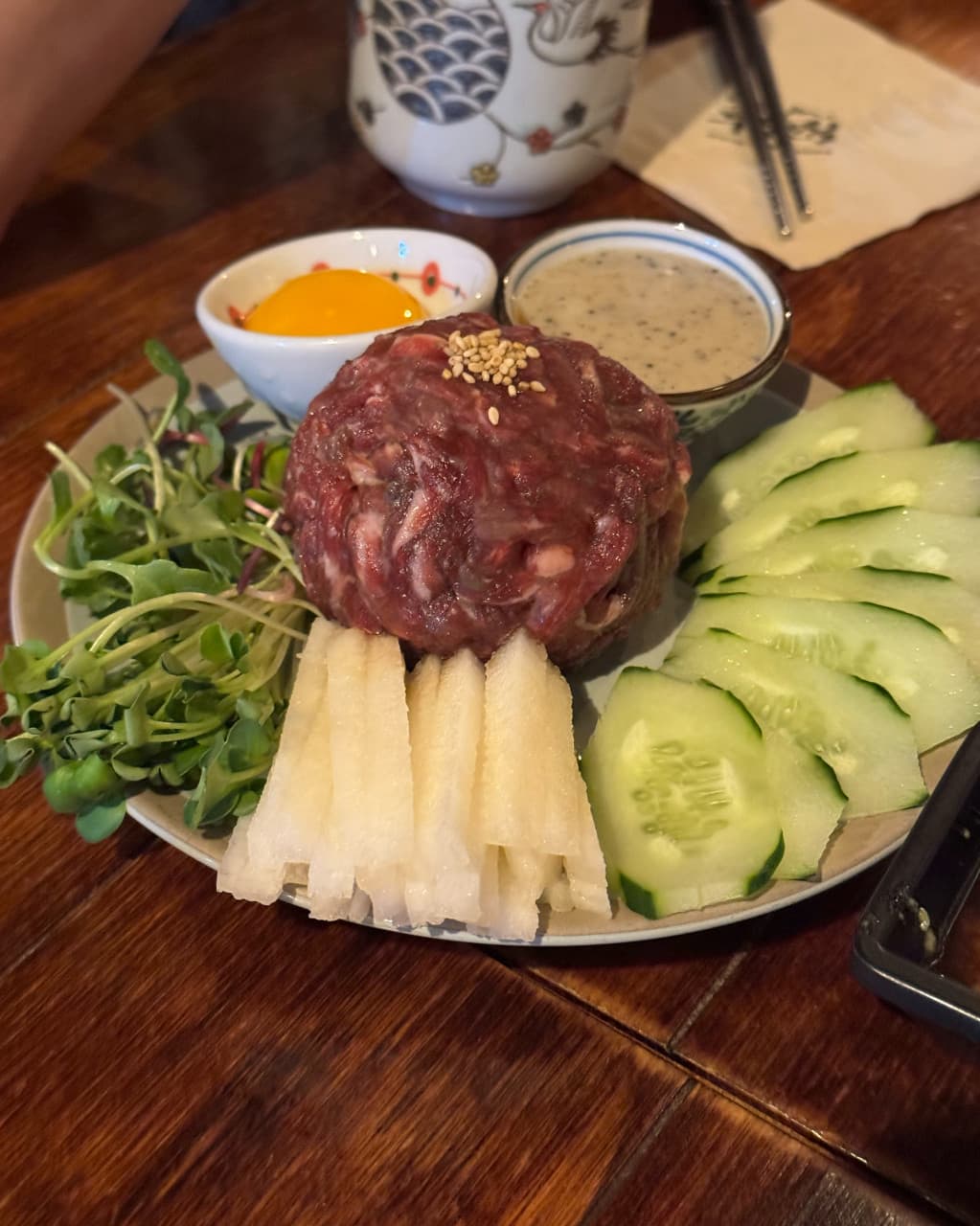 대전광역시 유성구 철길부산집 대전봉명점 요리주점 다찌석 혼술. 선홍빛 육회와 아삭한 배, 오이가 정갈하게 담긴 1인 안주가 노란 조명 아래 나무 테이블에 차려짐.
