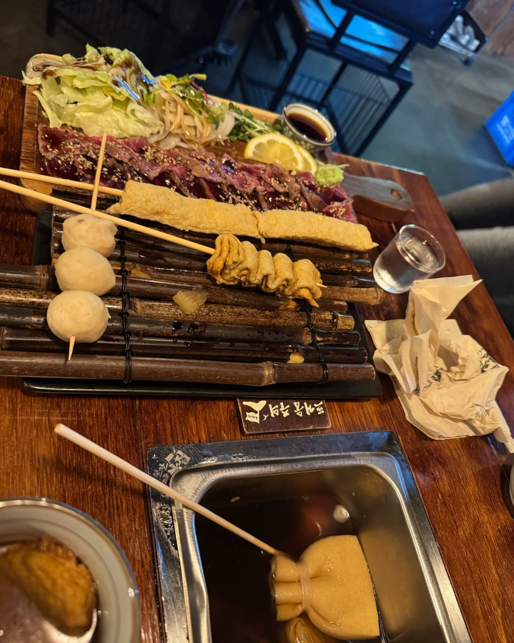 대전광역시 유성구 요리주점 철길부산집 대전봉명점 다찌석. 노란 조명 아래 소고기 타다끼와 대나무 발 위 어묵꼬치가 놓인 1인 혼술 상차림.