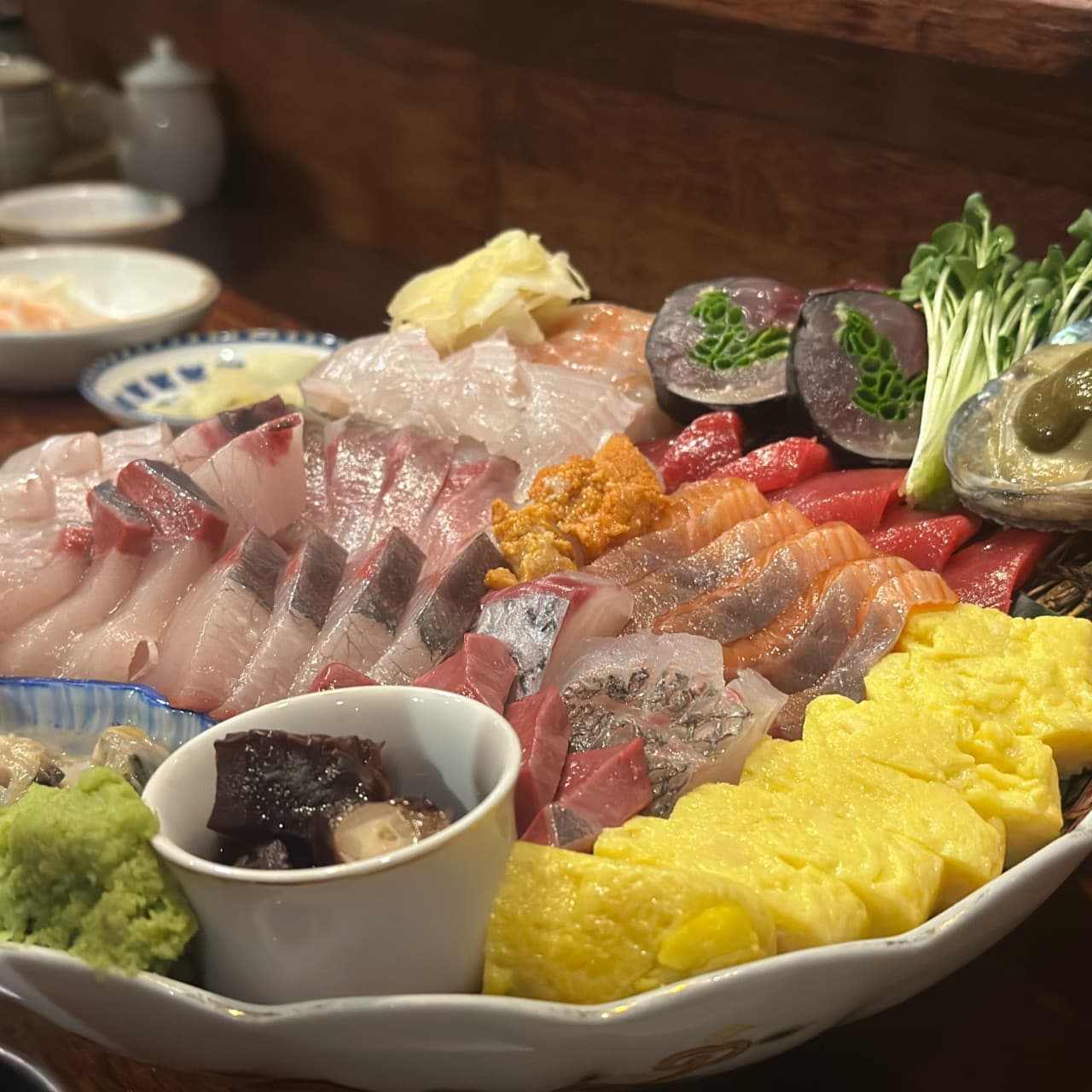 대전광역시 서구 천구네 대전 이자카야 다찌석 조명 아래 놓인 모둠 사시미. 윤기 나는 생선회와 성게알, 노란 계란말이가 조화로운 1인 혼술 메뉴.