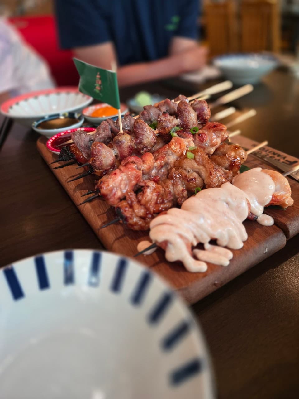 대전광역시 서구 이자카야 야키토리동작 대전가수원점. 노란 조명 아래 나무 판 위로 윤기 흐르는 꼬치구이와 소스가 차려진 다찌석 1인 혼술 상황.