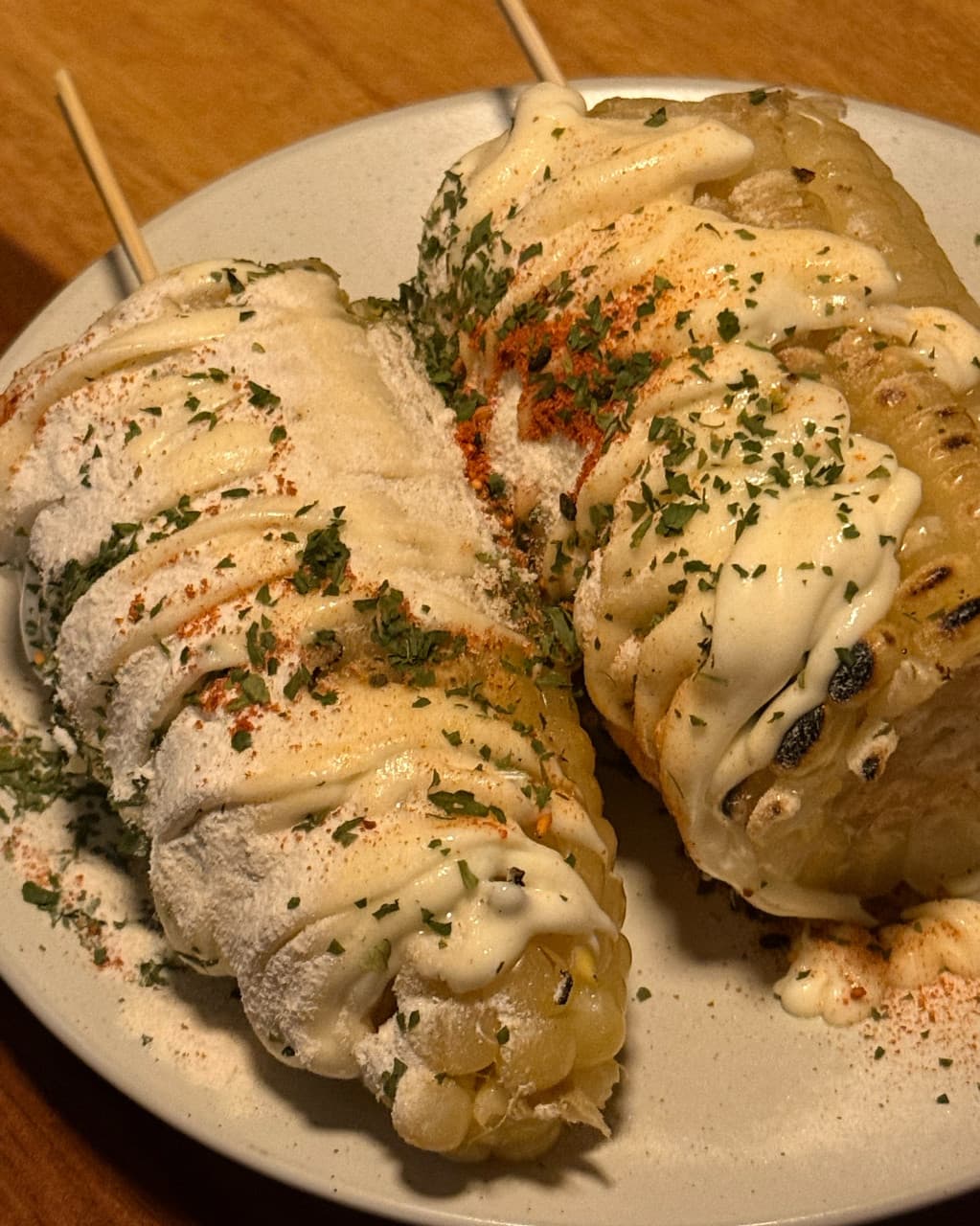 대전광역시 서구 혼술 이자카야 불오름 대전 다찌석의 1인 메뉴 옥수수 구이. 노란 조명 아래 치즈 가루와 마요네즈가 덮인 옥수수의 질감과 파슬리가 뿌려진 모습.