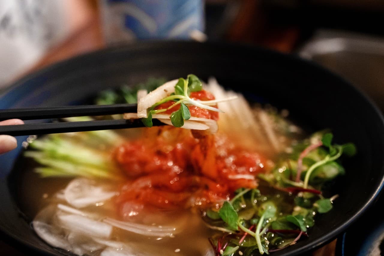 대전광역시 서구 혼술 요리주점 철길부산집 대전괴정점 - 다찌석 조명 아래 젓가락으로 집어 올린 선홍빛 육회와 채소가 담긴 물회 그릇의 질감.