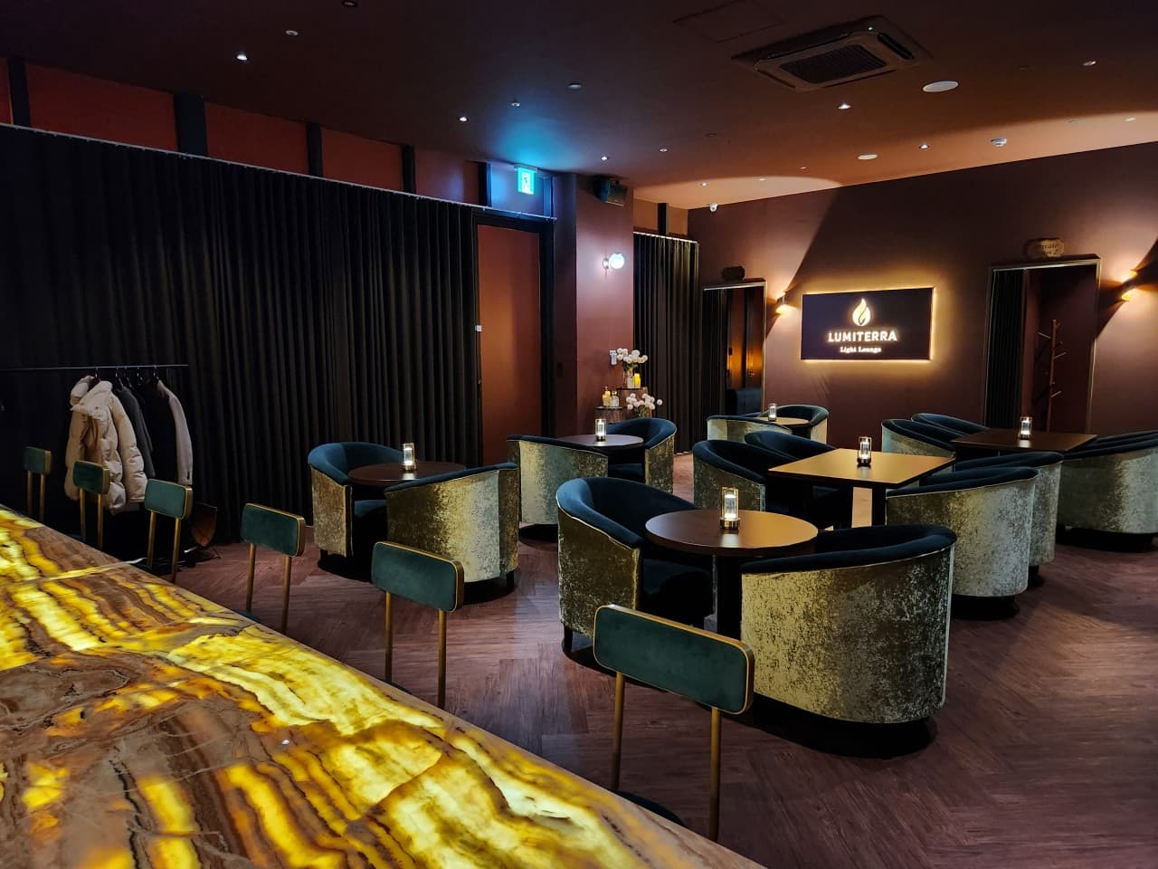 대전광역시 유성구 루미테라 대전 바(Bar). 빛이 투과하는 대리석 다찌석과 혼술용 벨벳 좌석이 배치된 내부. 낮은 조도의 조명 아래 1인석과 원형 테이블이 위치한 공간 구성.