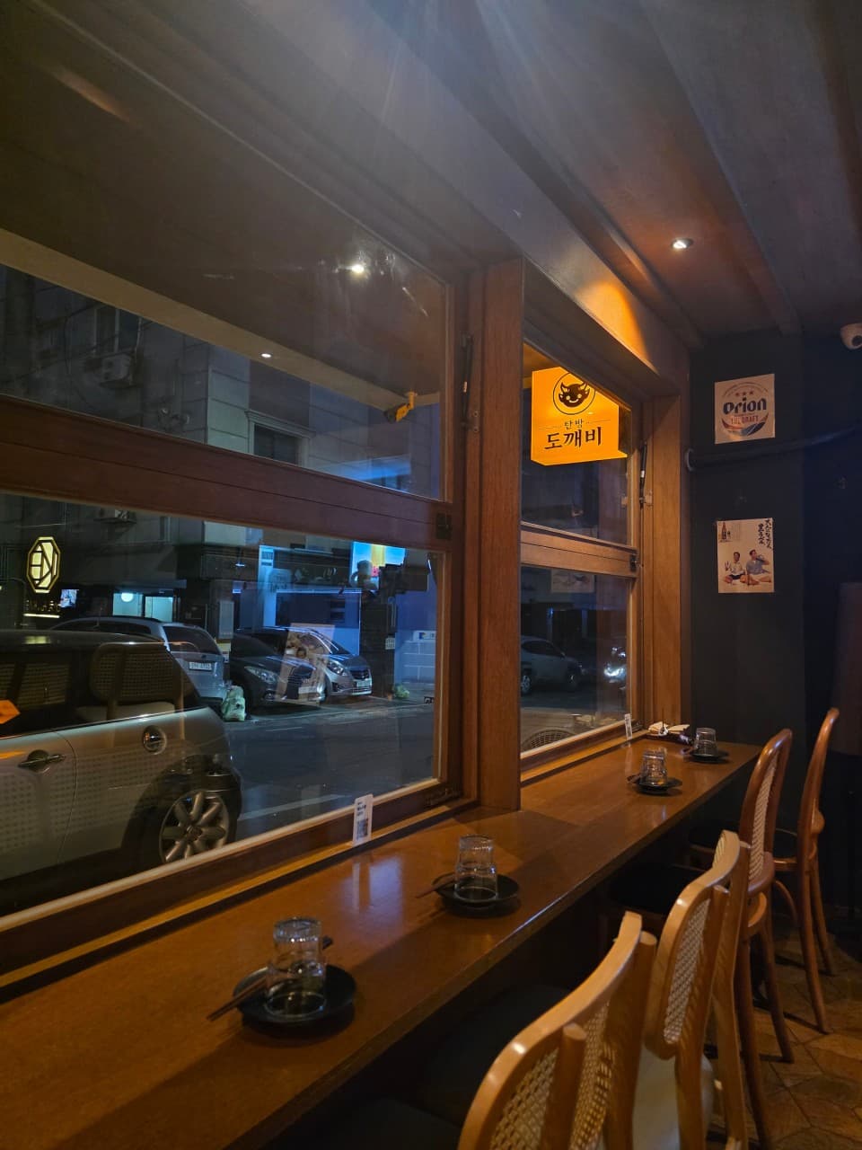 대전광역시 서구 탄방 도깨비 대전 이자카야 창가 다찌석. 주황빛 조명 아래 1인 혼술 식기가 세팅된 원목 테이블과 통유리 너머로 보이는 밤거리.