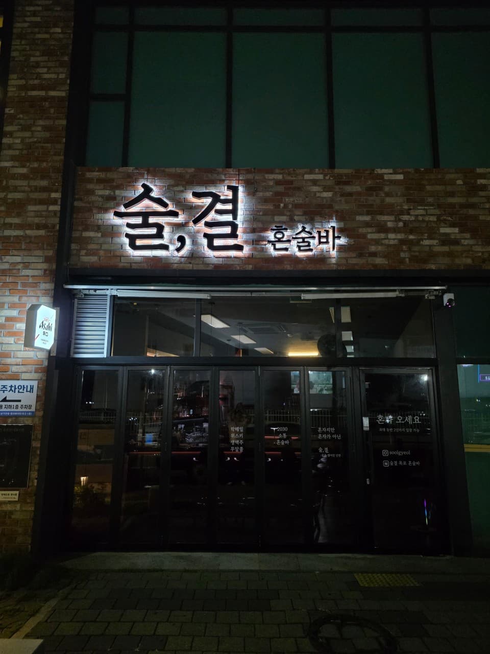 전남광주통합특별시 목포시 술결 목포혼술바 전남 바(Bar) 입구. 붉은 벽돌 외벽과 조명 간판 아래 1인 혼술 환영 문구가 적힌 유리문 사이로 실내 다찌석이 보이는 공간.