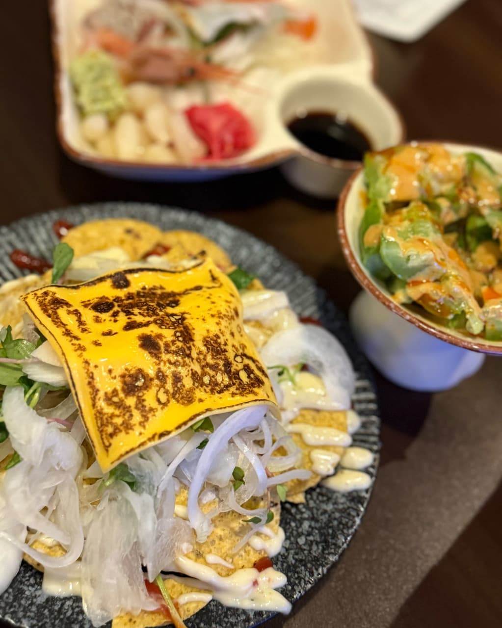 경상북도 구미시 이자카야 낼름 경북 1인 다찌석. 따뜻한 조명 아래 직화로 구운 체다치즈 나초와 신선한 사시미, 샐러드가 차려진 혼술 상황.