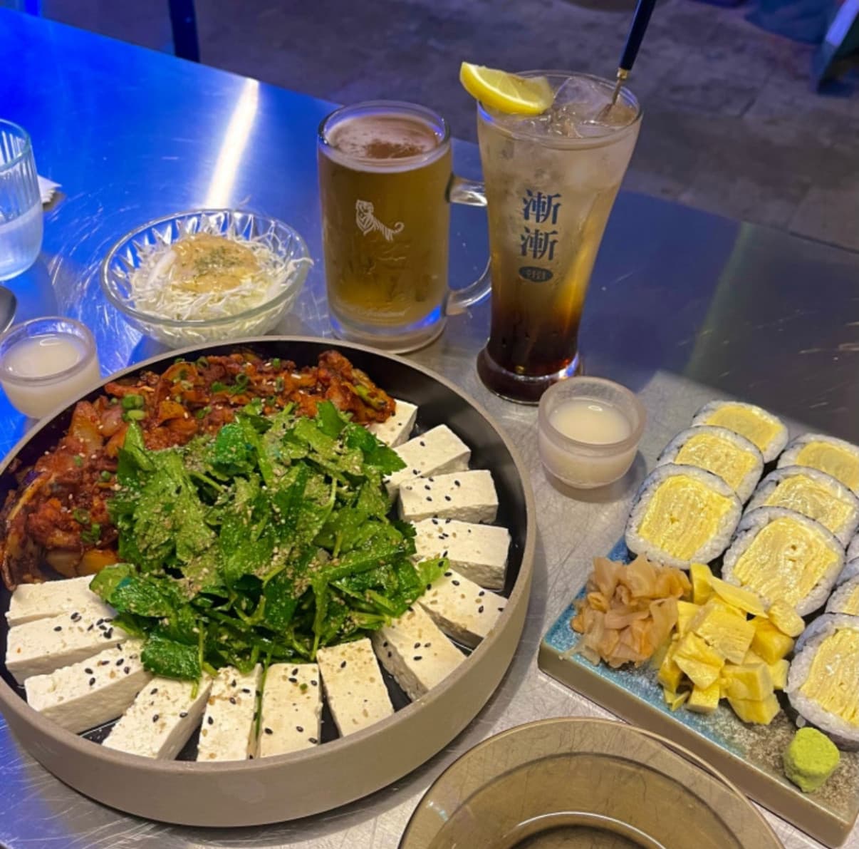 경상북도 경주시 점점 경북 요리주점 스테인리스 테이블 위 1인 혼술 차림. 푸른 조명 아래 두부 김치와 계란말이, 맥주와 하이볼이 놓인 다찌석 상황.