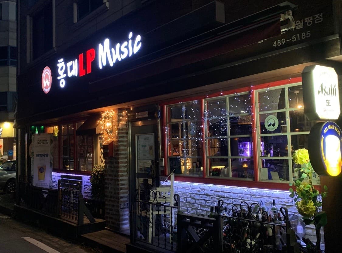 대전광역시 서구 홍대포차포차 대전 밤 외관. 전구 조명이 반짝이는 창가 다찌석과 벽돌 기둥 옆에서 1인 혼술을 즐길 수 있는 공간과 상황