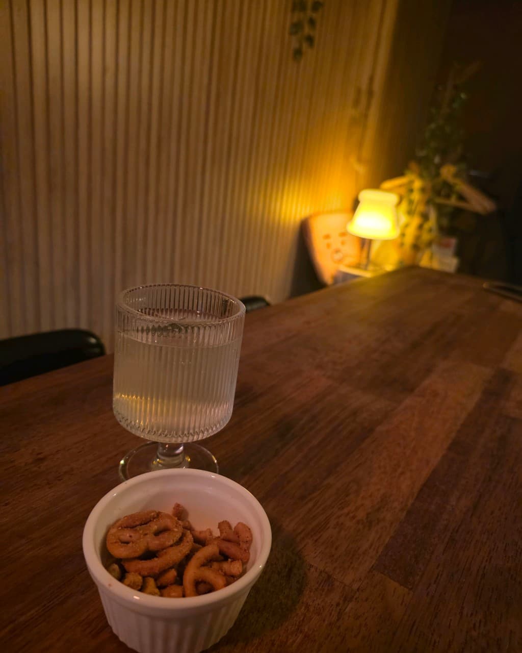 경상북도 경주시 둥지 혼술바 경북 바(Bar) - 노란 조명 아래 나무 다찌석에 차려진 투명한 술잔과 프레첼. 혼자 방문하는 1인석 테이블 상황을 묘사함.