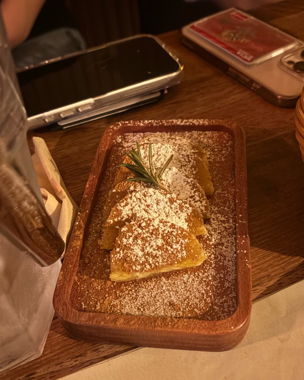 경상북도 경주시 둥지 혼술바 경북 바(Bar) 다찌석 노란 조명 아래 나무 트레이 위 시나몬 설탕 가루와 로즈마리가 얹어진 1인 안주. 혼술 중인 스마트폰이 놓인 테이블 구성.