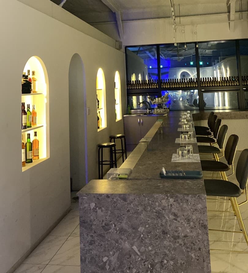 경상북도 칠곡군 여우bar 경북 혼술 바(Bar). 노란 조명이 비치는 아치형 벽 선반과 긴 석재 질감의 다찌석, 1인용 의자가 배치된 실내 전경.