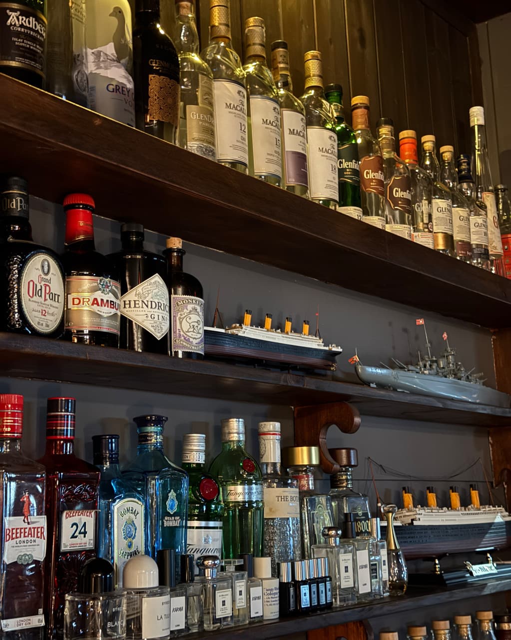 경상북도 안동시 레옹 정하점 경북 바(Bar)의 목재 선반 위 위스키와 진 병들. 혼술용 다찌석 앞 진열된 선박 모형과 조명을 받는 유리병의 질감.