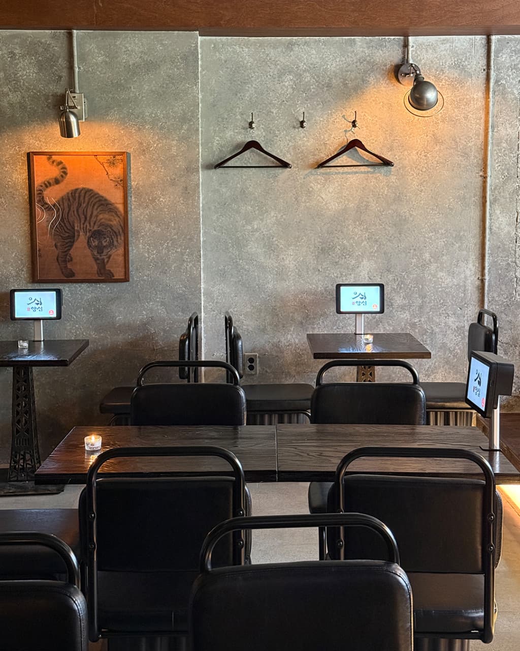 경기도 화성시 식사가되는 술집 양심 동탄점 경기 요리주점 - 노출 콘크리트 벽면 호랑이 그림 아래 태블릿이 설치된 1인 혼술 테이블과 핀 조명이 비추는 검은색 좌석 배치.