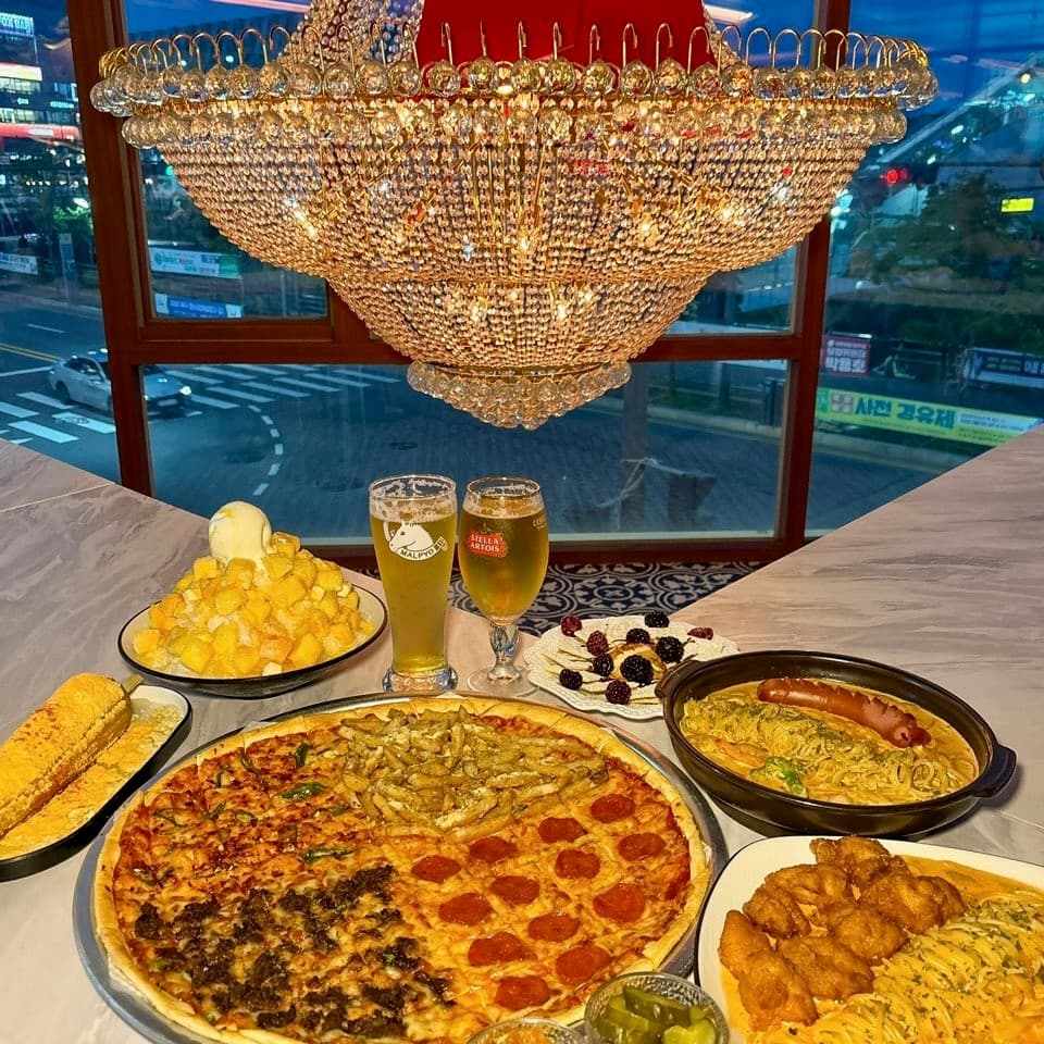 경기도 파주시 피맥당x레츠펍 파주야당본점 경기 요리주점 창가석. 크리스탈 샹들리에 아래 4가지 맛 피자와 생맥주, 망고 빙수가 차려진 테이블에서 즐기는 혼술 및 저녁 식사 상황.
