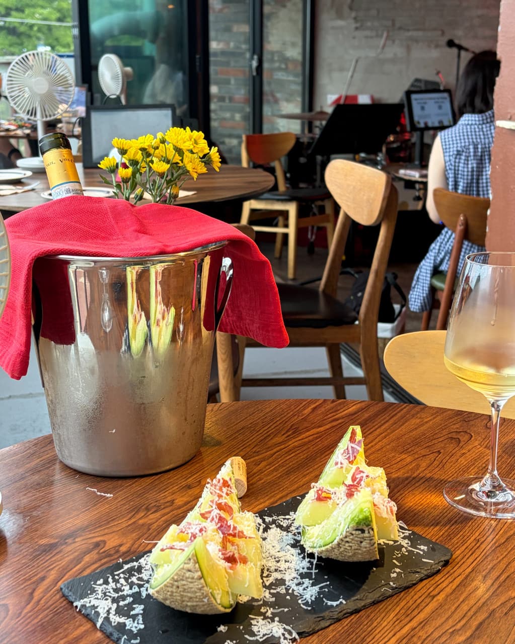 부산광역시 수영구 광안리남매 부산 와인 혼술. 나무 테이블 위 칠링된 와인과 치즈 가루가 뿌려진 멜론, 화이트 와인 한 잔이 놓인 1인석 조명 아래 상황.