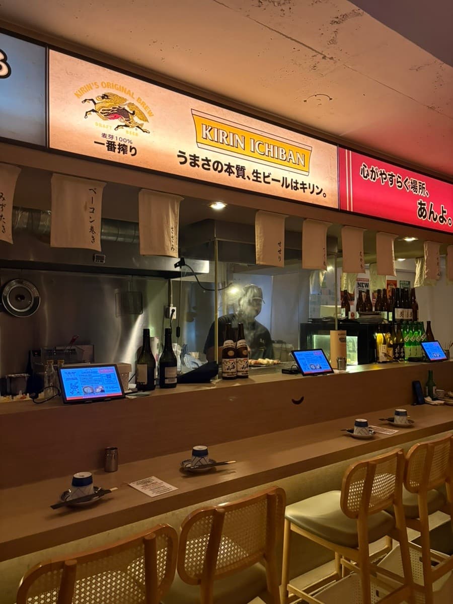 부산광역시 부산진구 요리주점 앙요 전포본점 부산. 기린 이치반 간판 아래 긴 다찌석과 1인 좌석마다 배치된 태블릿. 유리 너머로 연기가 피어오르는 조리 과정을 보며 즐기는 혼술 상황.