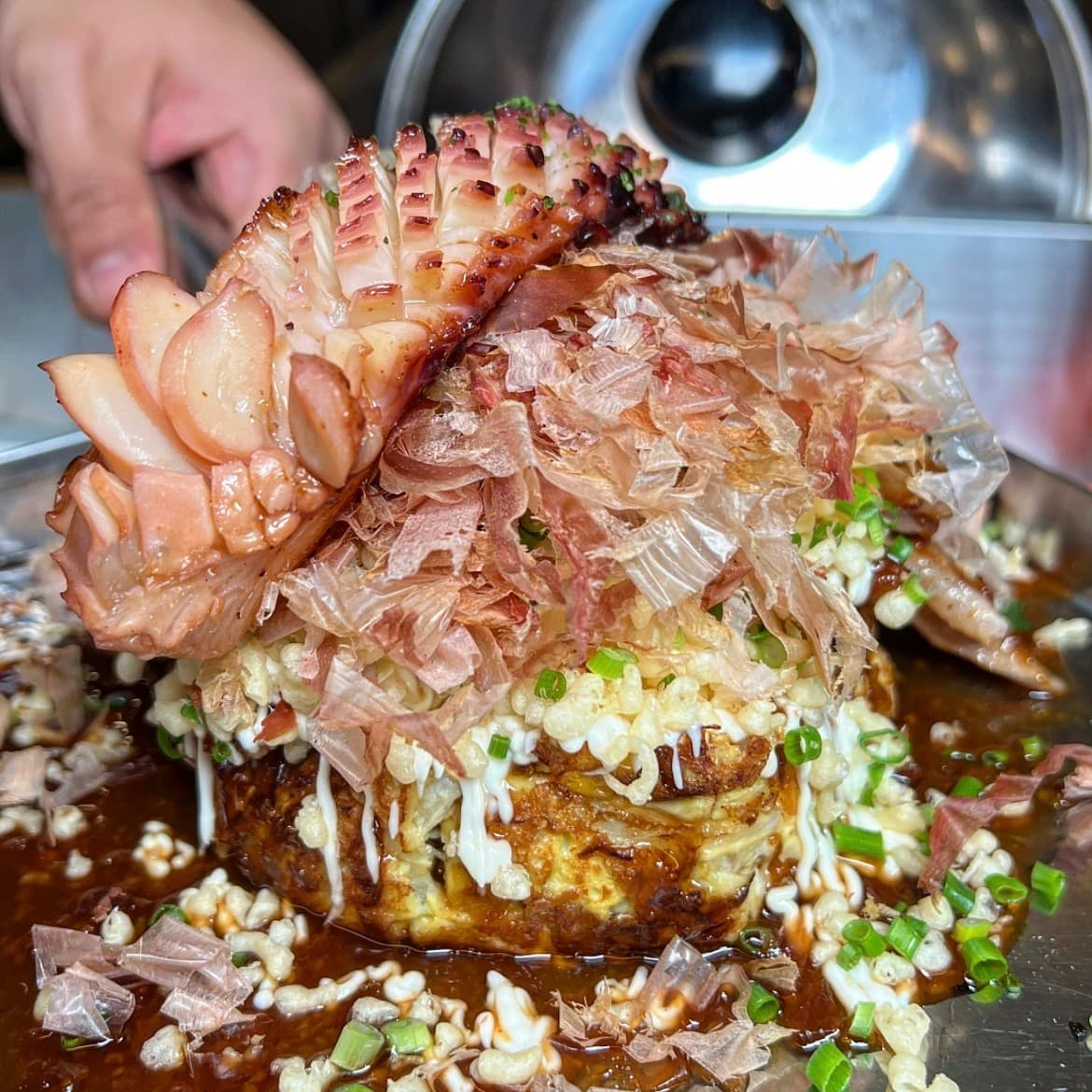 부산광역시 부산진구 야키야 본점 부산 이자카야 다찌석 혼술 상황. 철판 위 가쓰오부시와 구운 문어가 올라간 오코노미야키 질감과 조명을 받은 식재료가 강조됨.
