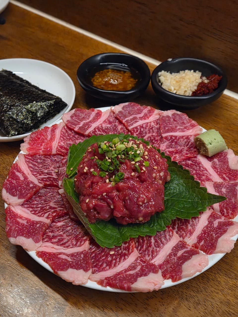 부산광역시 수영구 수달바 광안 부산 요리주점 다찌석에 차려진 육회와 사시미 세트. 나무 테이블 위 김과 마늘 소스가 곁들여진 1인 혼술 차림으로 고기의 질감이 선명함.