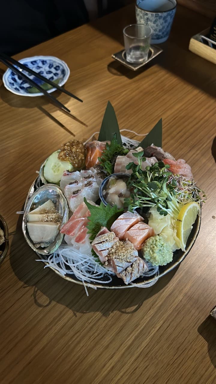 대구광역시 수성구 이자카야 야요이 신천시장본점 대구 나무 다찌석 조명 아래 놓인 1인 모둠 사시미. 전복과 연어의 질감이 강조된 혼술 상황.