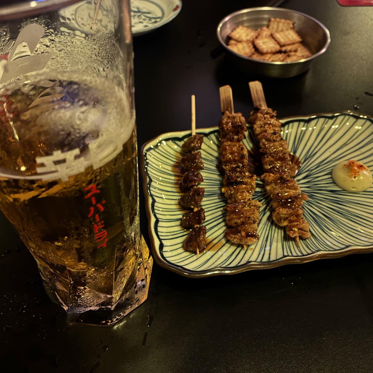 대구광역시 중구 요로이케 교동점 이자카야 혼술 - 어두운 조명 아래 다찌석에서 즐기는 탄산 가득한 생맥주와 노릇하게 구워진 닭꼬치 차림