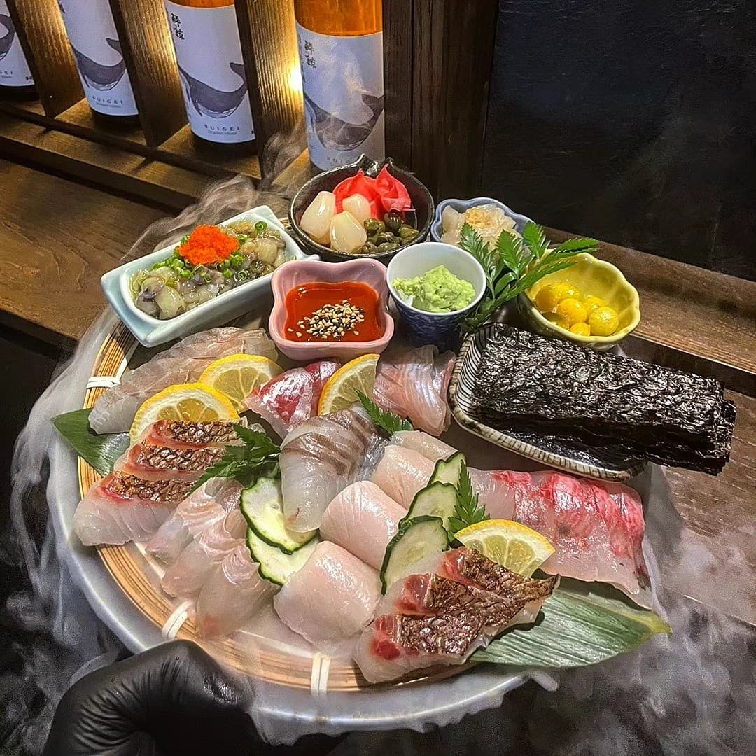 대구광역시 중구 이자카야 대담히 대구종로점 다찌석 1인 혼술. 드라이아이스 연기가 깔린 모듬 사시미와 사케 병이 놓인 바 테이블의 목재 질감과 노란 조명이 비치는 상황.