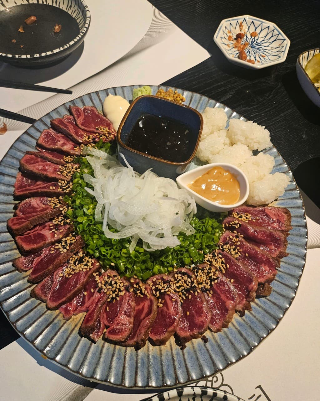 대구광역시 중구 이자카야 대담히 대구종로점 다찌석 조명 아래 1인 소고기 타다키와 밥, 양파가 차려진 상황. 선홍빛 육질과 참깨, 쪽파 질감이 강조된 혼술 메뉴 구성.